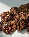 A pile of dark chocolate cookies with chopped nuts, arranged on a marble surface with soft shadows.