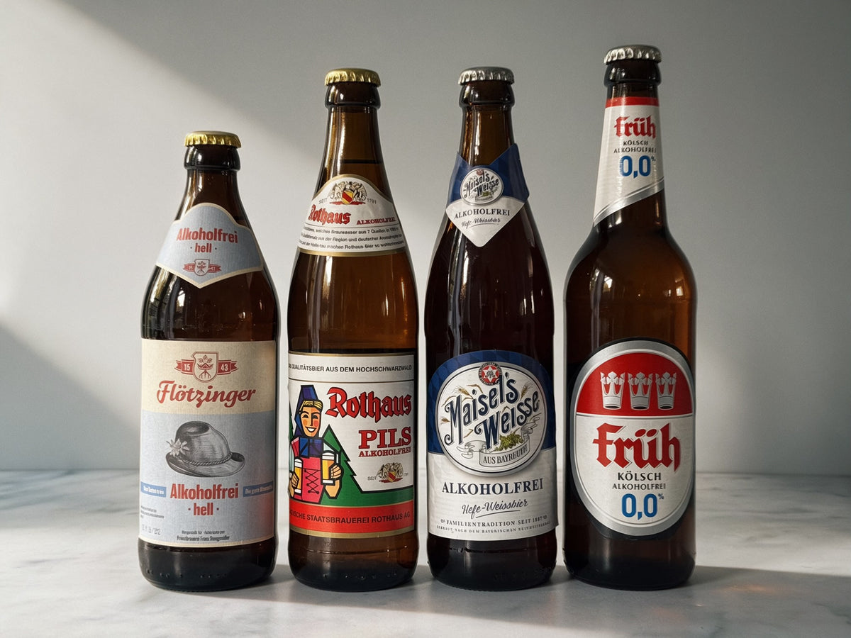 Four brown glass beer bottles with white labels, standing side by side on a light marble surface against a neutral background. The labels show different German beer brands and styles, including Flötzinger, Rothaus Pils, Maisel Weisse, and Früh Kölsch.