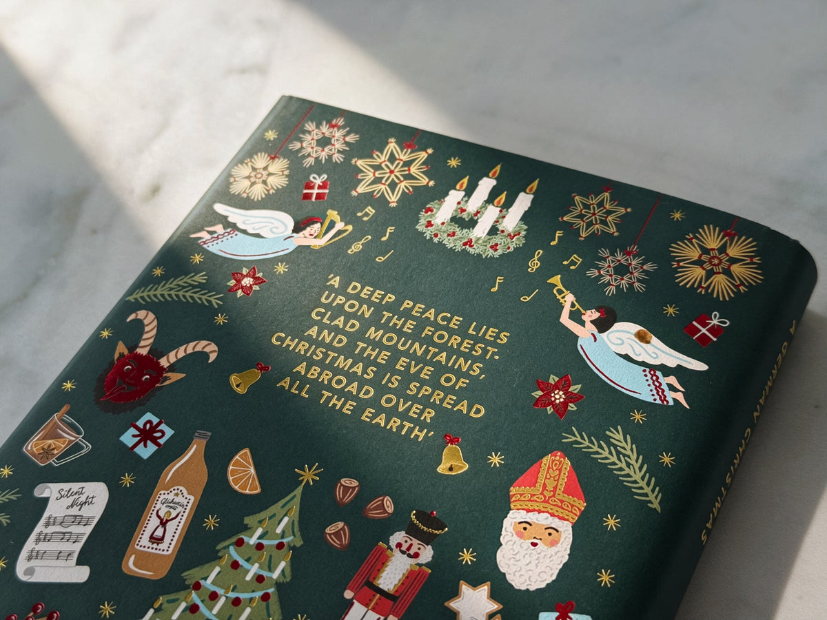 The rear of a dark green hardcover book with festive Christmas illustrations and a poem printed on the back in gold foil, photographed on a light marble surface with soft diagonal shadows.
