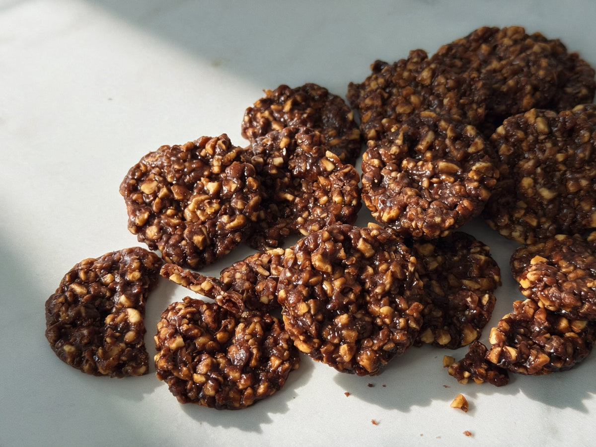 A pile of dark chocolate cookies with chopped nuts, arranged on a marble surface with soft shadows.