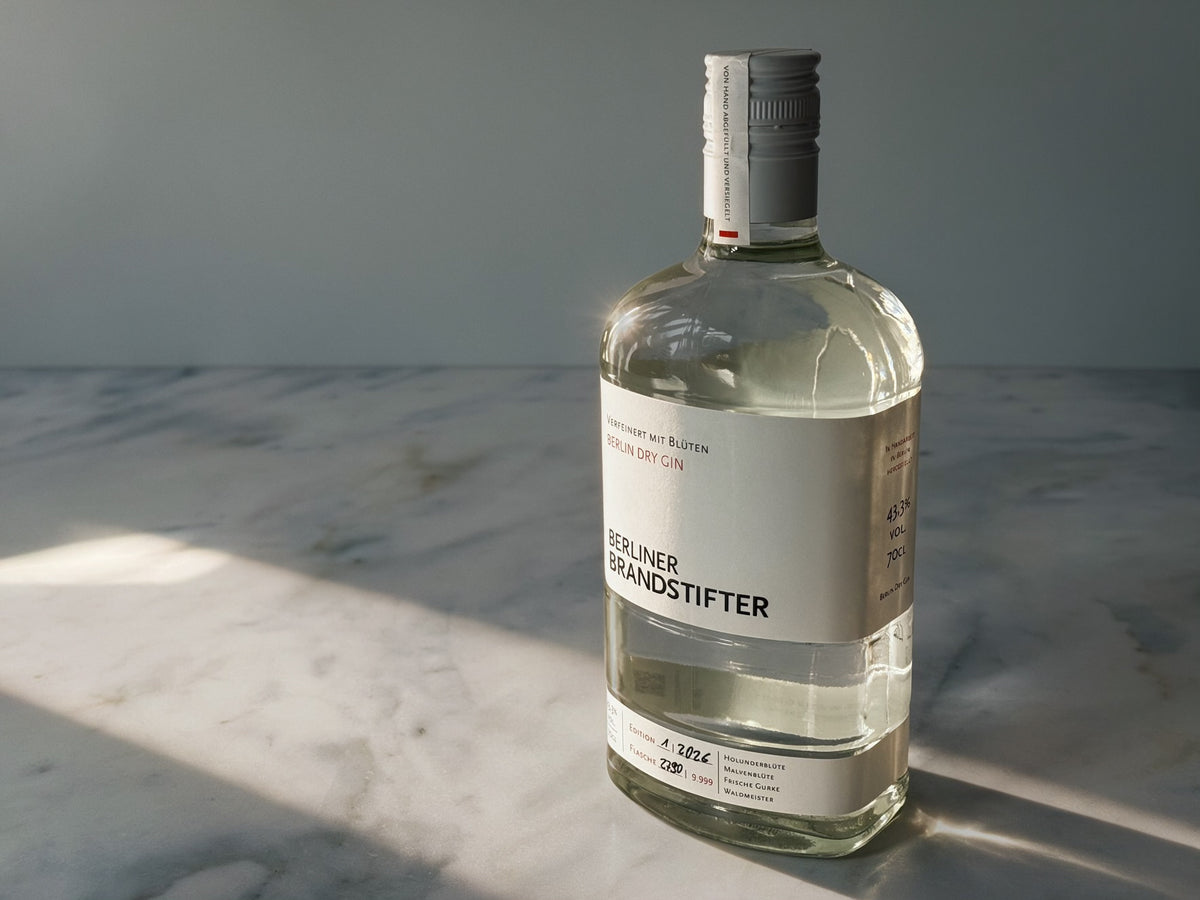 A bottle of Berliner Brandstifter gin on a white marble surface with dramatic diagonal sunlight casting shadows against a gray background.