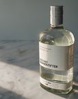 A bottle of Berliner Brandstifter gin on a white marble surface with dramatic diagonal sunlight casting shadows against a gray background.