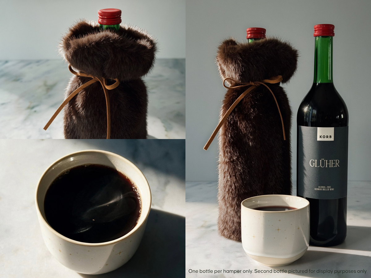 A dark brown faux-fur bottle cover shown wrapped around a wine bottle, with one bottle displayed upright and the other shown inside the cover. A small ceramic cup of mulled wine is also present on a light marble surface.